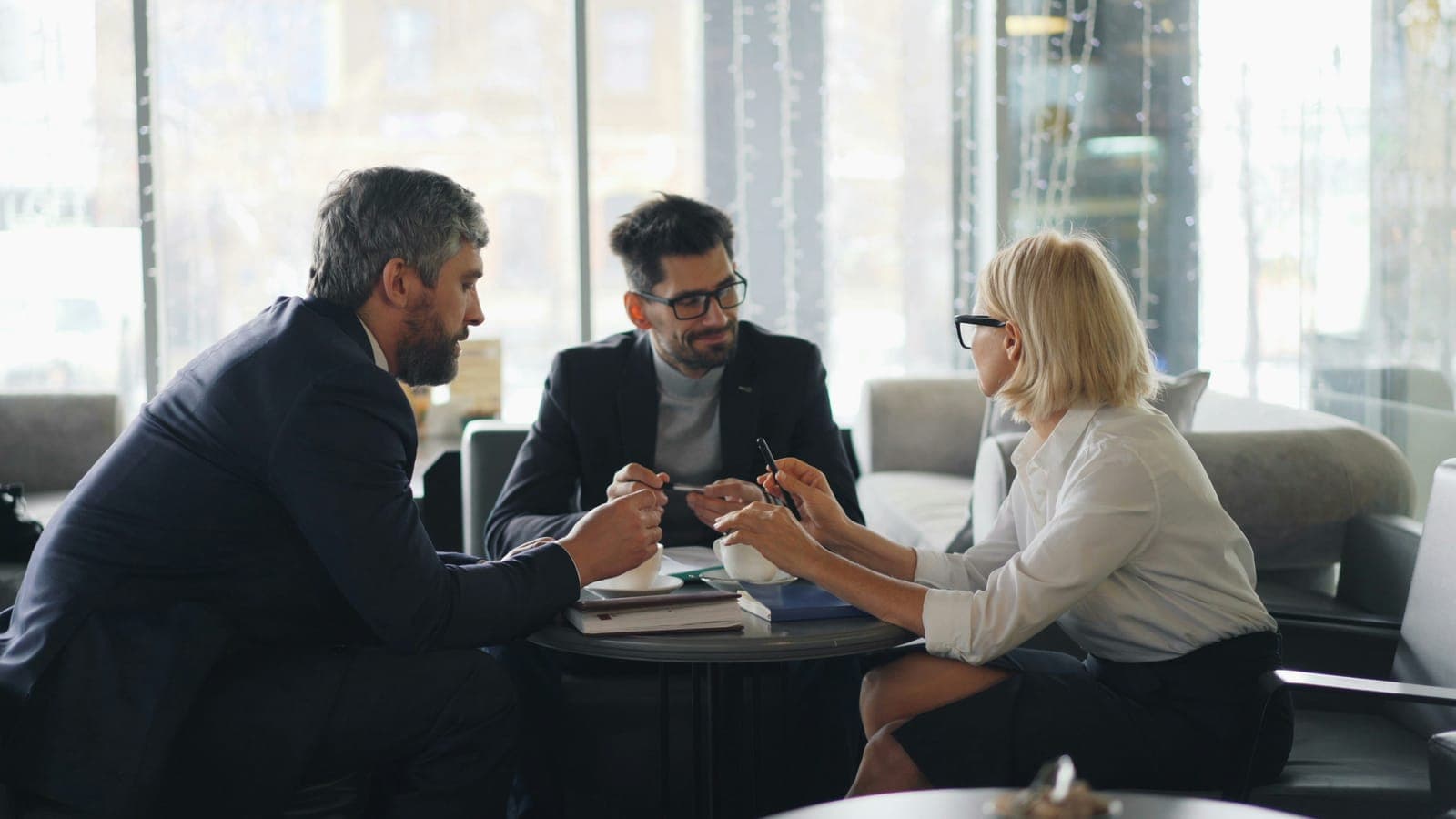 Three people in a meeting over coffee and documents